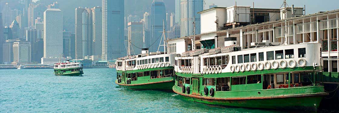 Green-and-white Star Ferry boats tied up at the pier, with the Hong Kong Island towers behind