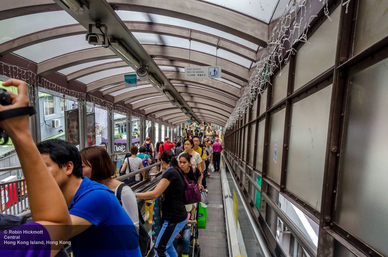 Riders on the covered Central-Mid-Levels escalator under a steep gradient sign