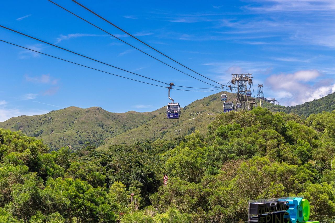 Ngong Ping 360 cable cars crossing green Lantau hillsides under a blue sky