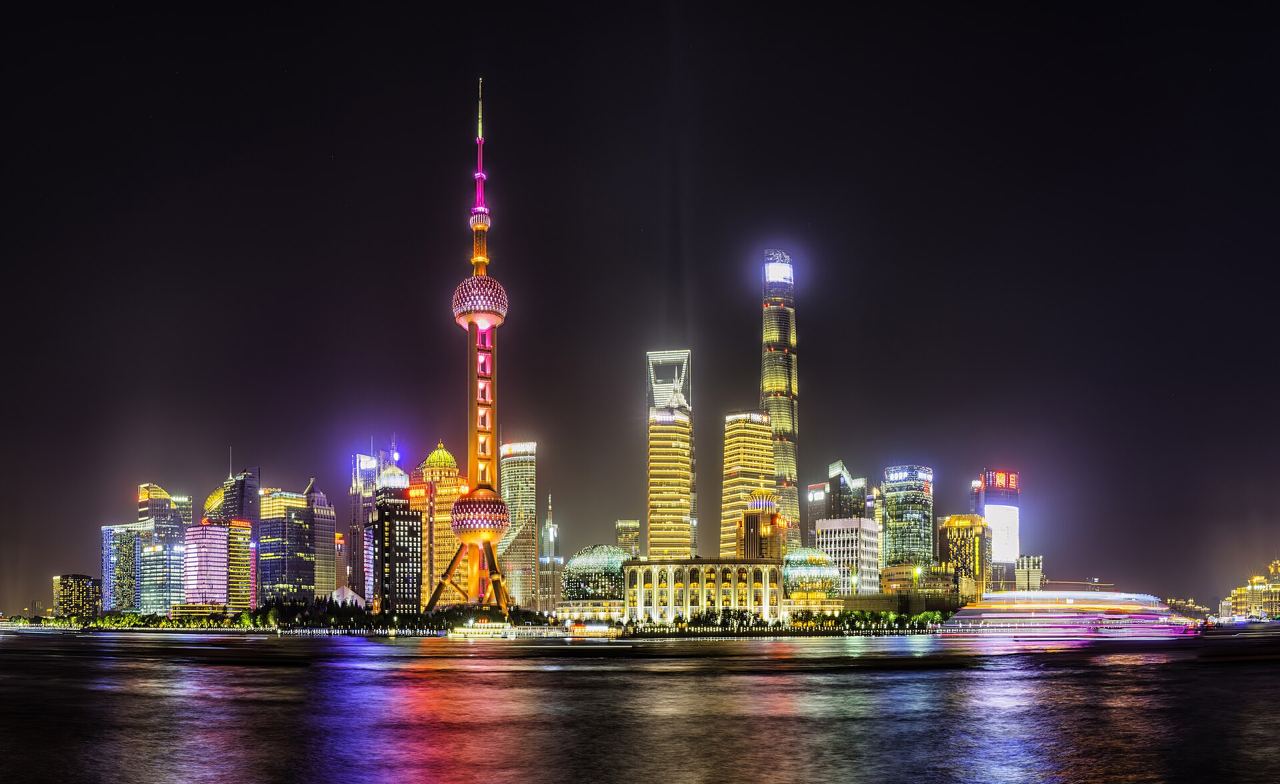 The lit-up Pudong skyline across the river at night, including the Oriental Pearl Tower and Shanghai Tower