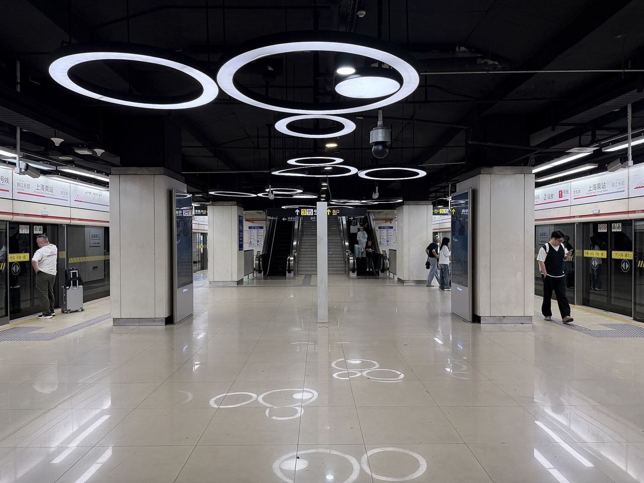 A quiet Shanghai Metro platform at Shanghai South Railway Station with a handful of riders near the escalators