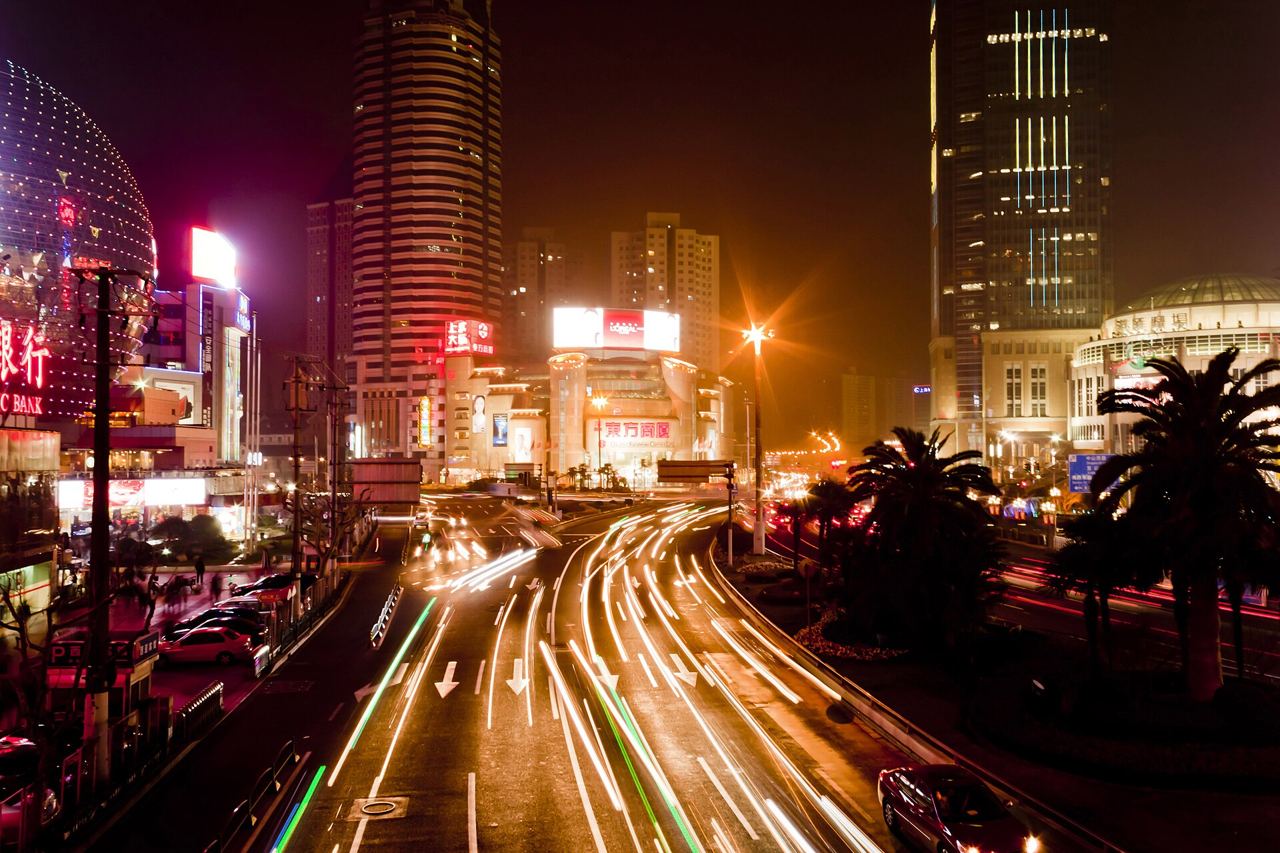 A long-exposure night view of the Xujiahui intersection in Shanghai with light trails from traffic and lit-up storefronts